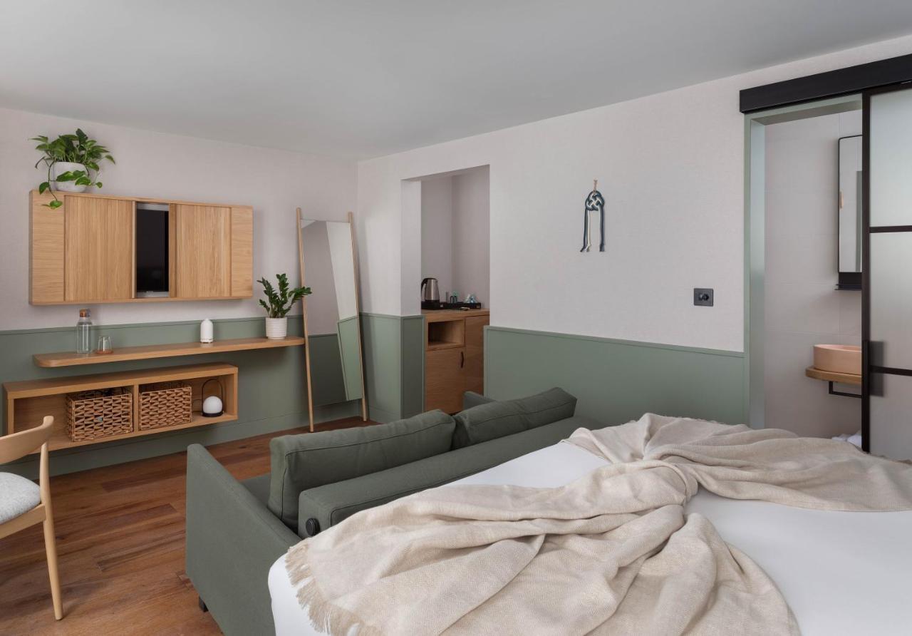 Inhabit Queen'S Gardens, A Member Of Design Hotels Londres Exterior foto The photo shows a modern, stylish room featuring a cozy and inviting atmosphere. The space includes a bed with a light-colored blanket draped over it, and a comfortable green sofa in the foreground. There is a wooden cabinet on the wall with greenery